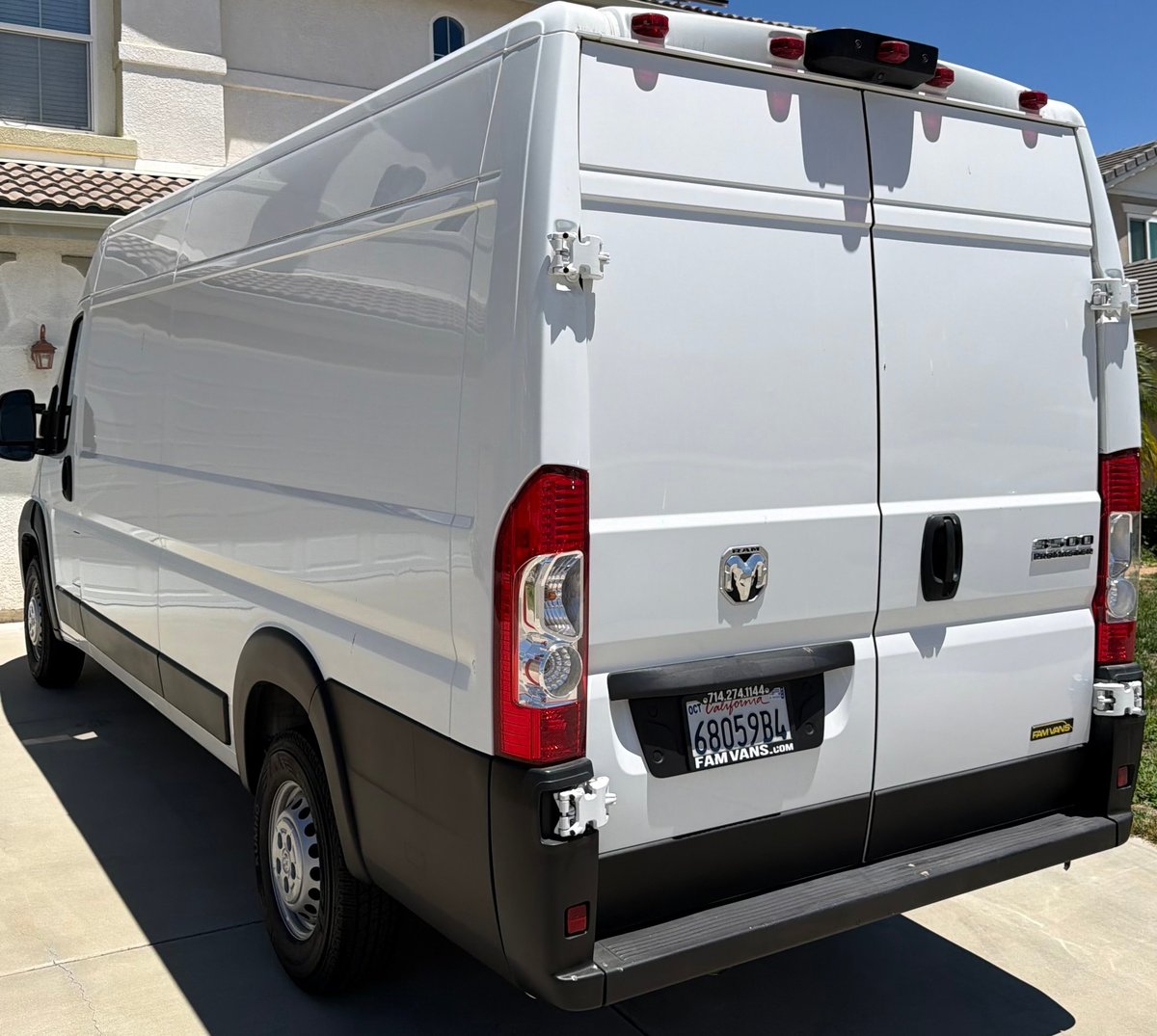 White and silver RAM commercial van parked in front of a residential building, rear view showing brake lights and license plate