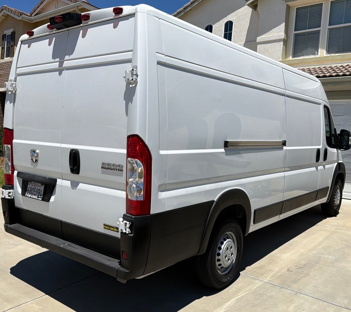 White Ram ProMaster cargo van rear three-quarter view in a residential driveway with red taillights visible